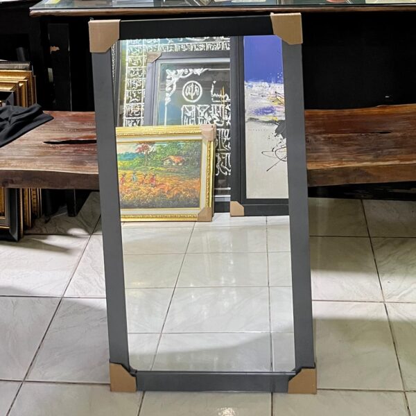kaca 50 x 80 Cermin dinding dengan bingkai hitam minimalis berdiri di lantai, siap untuk pemasangan, dikelilingi lukisan dan kaligrafi di sebuah galeri bingkai.